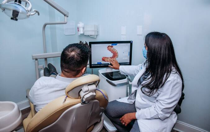 A Satisfied Woman After Dental Treatment Sits In Dental Chair And looks At The Dentist